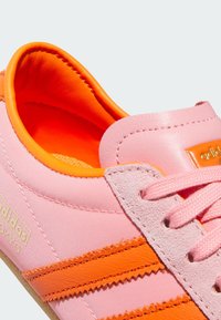 Adidași roz și portocalii cu un superior din pânză, accente din suede și două dungi portocalii. Dispun de o limbă căptușită și șireturi texturate.