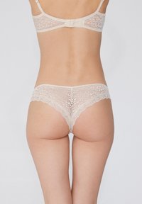 Lac at een lingerie-set in lichtbeige met een gekartelde rand, intrikate bloemenpatronen en een haak-en-oogsluiting aan de achterkant.