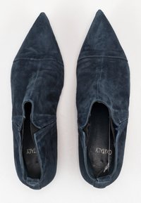 Zapatos de punta afilada en gamuza azul marino oscuro. Presentan un diseño de parte superior abierta con cortes en los laterales y un acabado suave y texturizado.