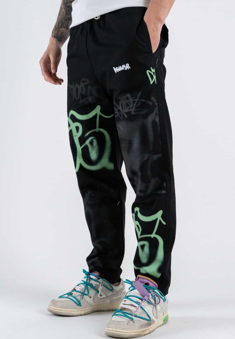 Pantaloni da jogging neri con grafiche verdi simili a graffiti e un logo bianco del marchio. Realizzati in tessuto morbido, con vita elastica e tasche.
