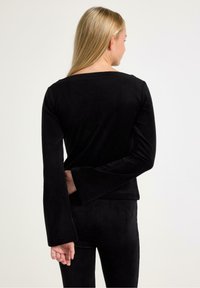 Svart velour långärmad topp med bred rund halsringning och utsvängda ärmslut, figursydd vid midjan, slät textur, bärs med matchande byxor.