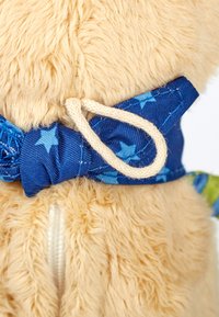 Beiger Plüschstoff mit weicher Textur, verziert mit einem blauen Sternenmusterband, das mit einem beigen Seil gebunden ist. Reißverschlussdetails sind am Körper sichtbar.