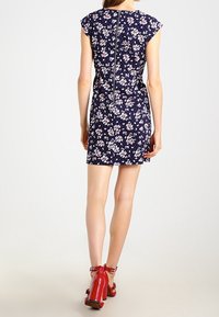 Navy floral dress with short cap sleeves, back zipper, and fitted silhouette; paired with red high-heeled sandals.