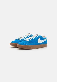 Zapatillas de ante azul con el swoosh blanco de Nike, cordones crema y suela de goma marrón. Presenta un diseño clásico y material texturizado.