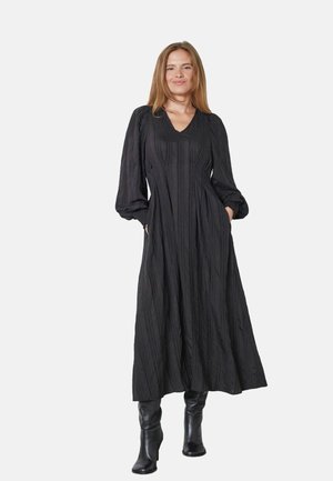 Črna maxi obleka z dolgimi manšetami in V-izrezom. Ima teksturirano blago in dve stranski žepki, v kombinaciji z črnimi škornji do kolen.