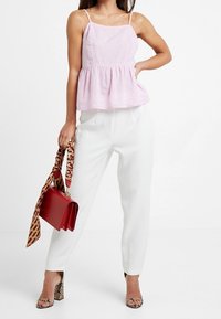 Top peplum rosa chiaro con spalline sottili, pantaloni bianchi su misura, borsa rossa e tacchi con stampa rettile. Texture lisce con dettagli sottili.