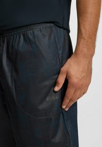 Zbliżenie na dłoń spoczywającą na ciemnoniebieskich szortach sportowych z subtelnym wzorem w kratkę i elastycznym pasem.