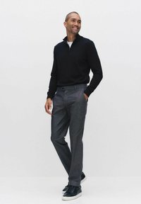 Svart zip-hals-tröja, grå byxor och mörka sneakers. Outfitten har en figurnära design med släta texturer och rena linjer.