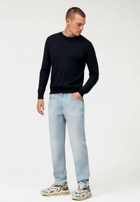 Maglione blu navy, jeans azzurri e scarpe da ginnastica multicolori. Il maglione ha una scollatura rotonda; i jeans sono a gamba dritta. Look casual.