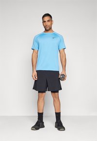 Heledad sinine Nike spordit-särk, mustad lühikesed püksid, mustad sokid ja tennisetossud. Hoides käes musta raskust. Lihtne disain, hingav kangas.