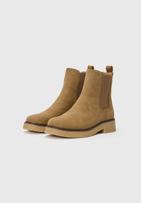 Botas cortas de ante marrón con paneles laterales elásticos, puntera redonda y suela de goma clara en contraste. Presentan lengüetas para facilitar su uso.