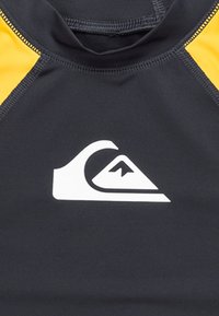 Svart våtdräkt med gula accenter, som har en framträdande vit logotyp. Slät yta och atletisk passform designad för vattensporter.