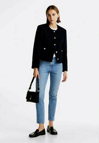 Ναυτικό μπλε σακάκι με χρυσά κουμπιά, φορεμένο πάνω από ένα λευκό πουκάμισο, συνδυασμένο με ανοιχτό μπλε τζιν και μαύρους λουστρίνια. Μικρή μαύρη τσάντα χειρός.