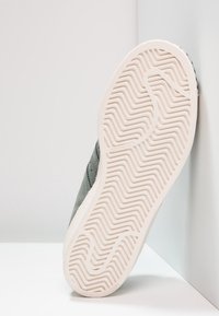 Zapatilla de ante gris con suela de goma texturizada; la suela presenta un patrón de agarre en zigzag y un borde blanco. Diseño minimalista, vista en ángulo.