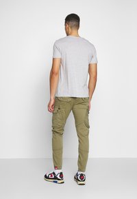 Grijze t-shirt, olijfgroene cargo-broek met zakken en zwarte sneakers met rode en blauwe accenten. Casual outfit gezien vanuit de rug.