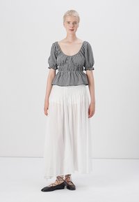 Top peplum în carouri alb-negru cu mâneci bufante, purtat cu o fustă maxi albă fluida. Pantofi negri cu talpă joasă și bretele încrucișate.