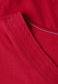 Tissu en coton rouge au toucher lisse, présentant un décolleté en V et des surpiqûres bleu clair contrastantes le long des bords.
