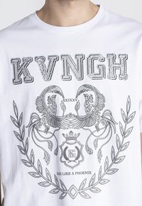 Biała koszulka z bawełny, z czarną grafiką przedstawiającą dwa feniksy, tekstem "KVNGH" oraz dekoracyjnymi gałązkami laurowymi.