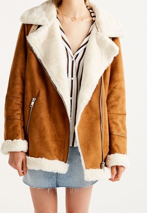 Frau trägt eine braune Jacke mit Teddyfellfutter, ein gestreiftes Hemd mit Knöpfen und einen hellblauen Jeans-Minirock.