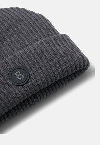 Grijze gebreide beanie met ribbeltextuur en een brede omslag. Bevat een ronde zwarte tag met een witte "B" logo. Zacht materiaaloppervlak.