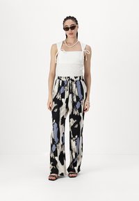 White, smocked tank top with tie straps, paired with black and cream wide-leg pants featuring abstract blue and black patterns. Black sandals.
