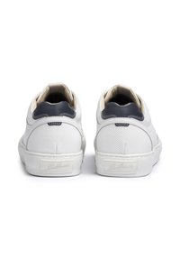 White leather sneakers with navy accents, textured perforated upper, and a flat rubber sole. Features a padded collar and branded heel tab.