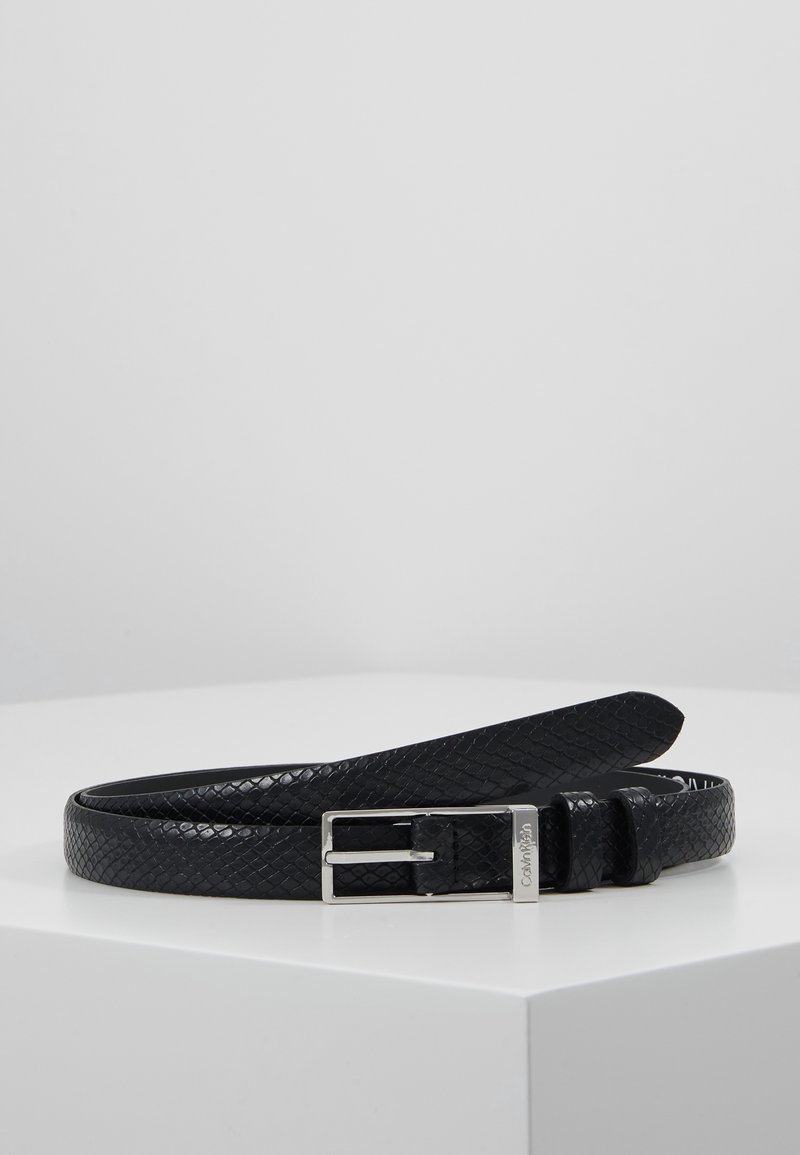 Ceinture en cuir noir texturé avec boucle rectangulaire argentée posée à plat sur une surface blanche.