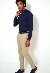 Marineblauw shirt met lange mouwen en knopen, gecombineerd met beige chino's en zwarte sneakers. De outfit is aangesloten en casual, met een geweven zwarte riem.