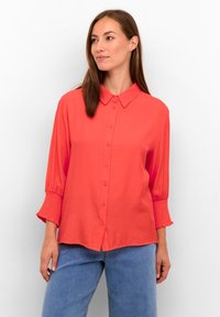 Camicetta corallo con maniche lunghe arricciate e colletto classico. Realizzata in tessuto liscio, presenta una vestibilità rilassata e un colore unito.