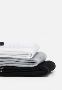 Tri par socks: bijele na vrhu, svijetlosive u sredini i crne na dnu. Imaju glatku teksturu i uvijene rubove.
