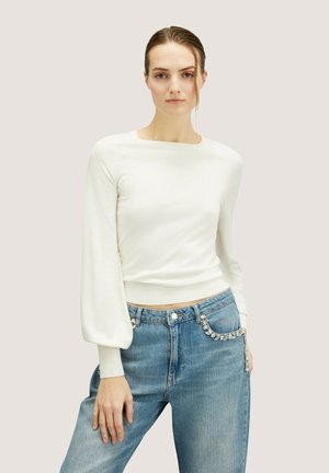 Witte geribbelde langesleeve top met een vierkante halslijn en pofmouwen, gecombineerd met casual blauwe jeans met een met juwelen versierde zijzak.