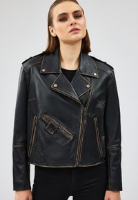 Giacca da biker in pelle nera con accessori in argento, tasche con zip e colletto strutturato. Presenta cuciture a contrasto e un design accorciato.
