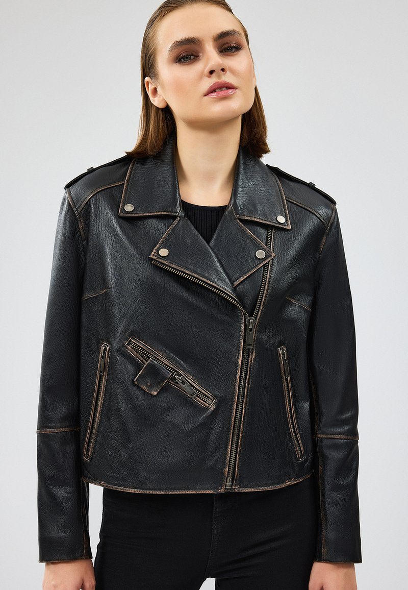 Giacca da biker in pelle nera con accessori in argento, tasche con zip e colletto strutturato. Presenta cuciture a contrasto e un design accorciato.