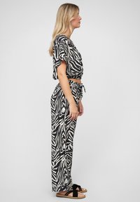 Melna un bēša zebras raksta divdaļīgs kostīms ar īsu topu un brīviem biksēm, kurām ir elastīga josta un aukla.