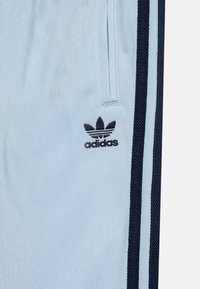 Pantaloni sportivi azzurri con strisce laterali blu scuro, con un piccolo logo nero Adidas sulla coscia sinistra. Tessuto dalla texture liscia.