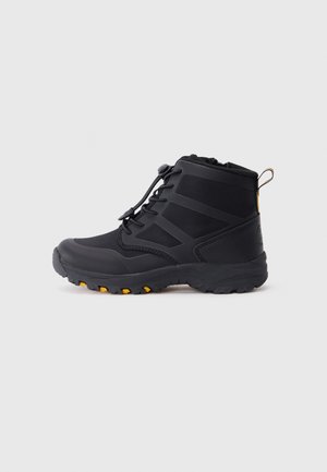 Bota impermeável preta com superfície texturizada, apresentando um fecho de atacadores, colarinho acolchoado e detalhes amarelos na sola e no calcanhar.