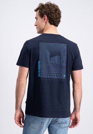 Mężczyzna zwrócony tyłem, ubrany w granatowy t-shirt z geometrycznym niebieskim nadrukiem architektonicznym oraz tekstem "GABBIANO" na plecach.