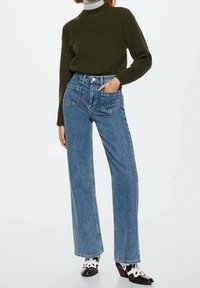 Suéter verde de punto, jeans de pernera ancha azul de tiro alto con dos bolsillos delanteros, tela texturizada, combinado con zapatos de tacón blanco y negro.