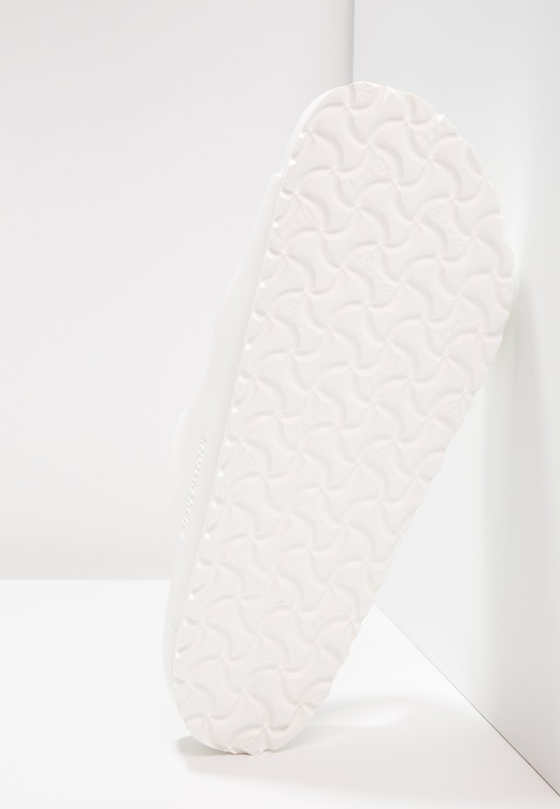 Suola di scarpa bianca con un motivo a onde testurizzato, leggermente curvata e bordi lisci. Leggero marchio impresso di lato.
