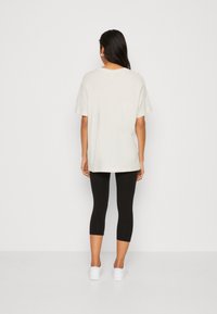 Ljusgrå oversized t-shirt med korta ärmar, kombinerad med svarta capri leggings och vita sneakers, visad mot en enkel bakgrund.