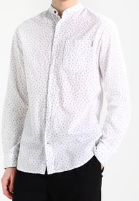 Vit långärmad skjorta med knapp-up och ett litet mönstrat tryck. Har en bandkrage och bröstficka. Tillverkad av lättviktigt tyg.