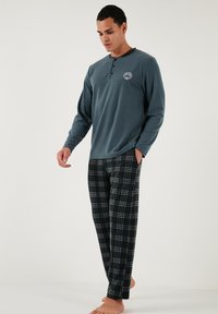 Garais piedurkņu teāla tops ar pogājamu kaklu, apvienots ar melniem un baltiem pārklātiem pidžamu biksēm. Mīksta auduma, brīvā piegriezumā un ar kabatām.