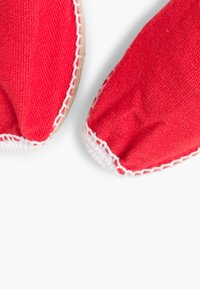 Chaussures en textile rouge avec des coutures blanches autour des bords, présentant un bout rond et une texture douce et flexible.