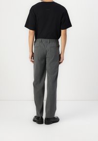 T-shirt nera a maniche corte abbinata a pantaloni grigi a righe sottili, con cintura elastica e due tasche posteriori. Si indossano scarpe nere.