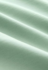 Tela verde menta clara con una textura suave, que presenta pliegues visibles y un patrón de tejido uniforme. Apariencia suave y ligera.