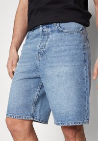 Lyseblå denimshorts med fem lommer, knaplukning og falmet tekstur, der slutter lige over knæet.