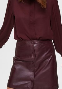 Burgundy leather skirt with a front button closure and a smooth texture, paired with a matching blouse featuring a ribbed design.