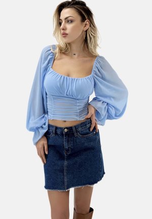 Hellbluse mit puffartigen Ärmeln und geraffter Textur, kombiniert mit einem kurzen Jeansrock mit fransigem Saum.