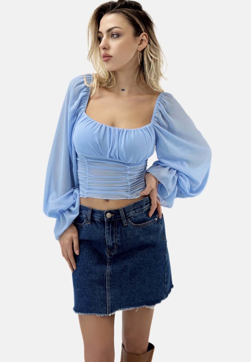 Hellbluse mit puffartigen Ärmeln und geraffter Textur, kombiniert mit einem kurzen Jeansrock mit fransigem Saum.