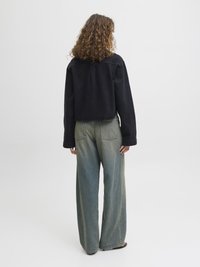 Svart kort jakka med avslappnad passform, ihop med vida ljusblå denimjeans med en urtvättad textur och bakfickor.